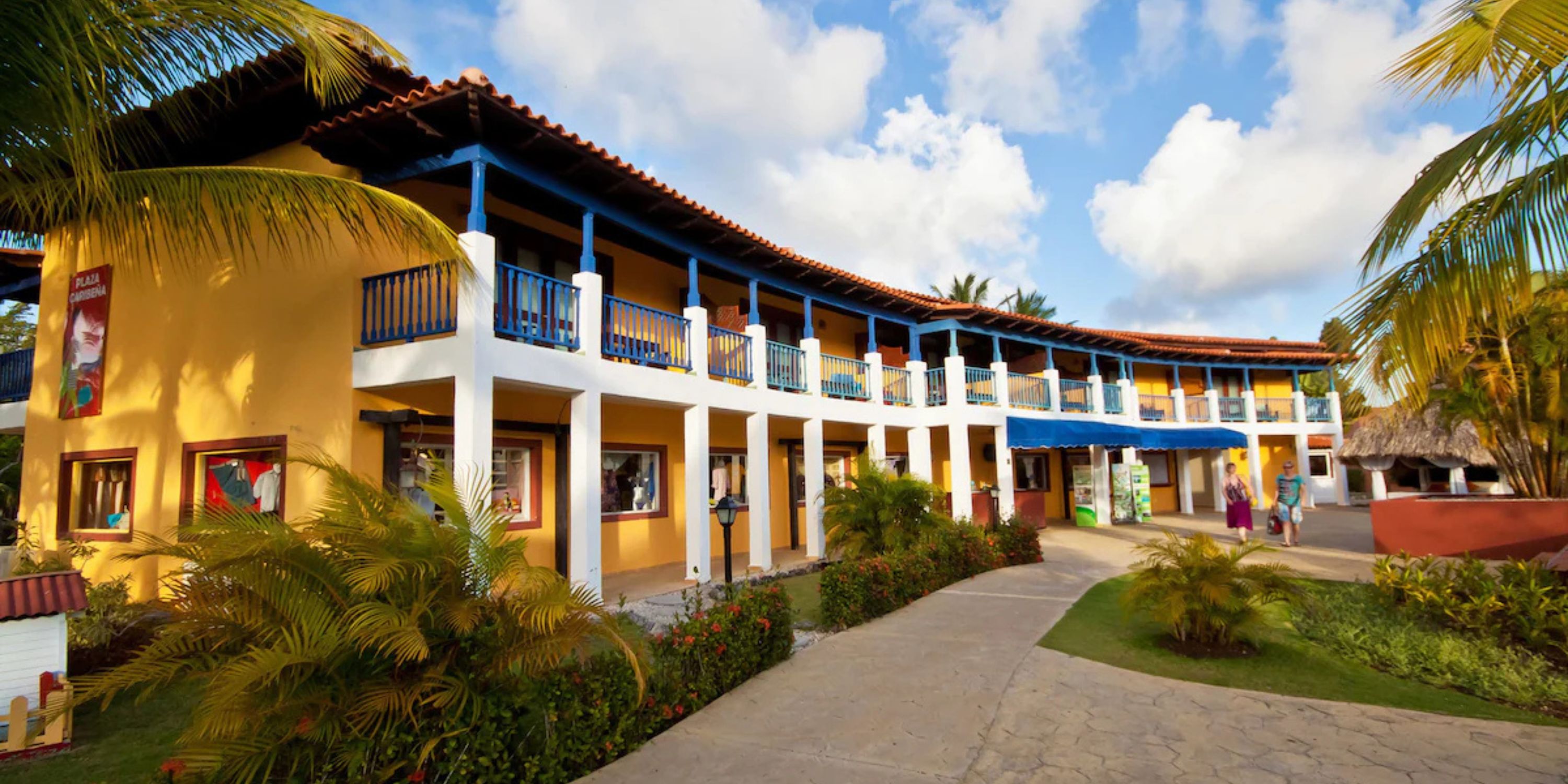 Catalonia Bayahibe: Ideal destination wedding spot with two-story yellow building, blue railings, and palm trees.