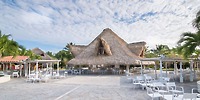 Catalonia Bayahibe: open-air restaurant with thatched roof, palm trees, white chairs&mdash;ideal for a destination wedding.