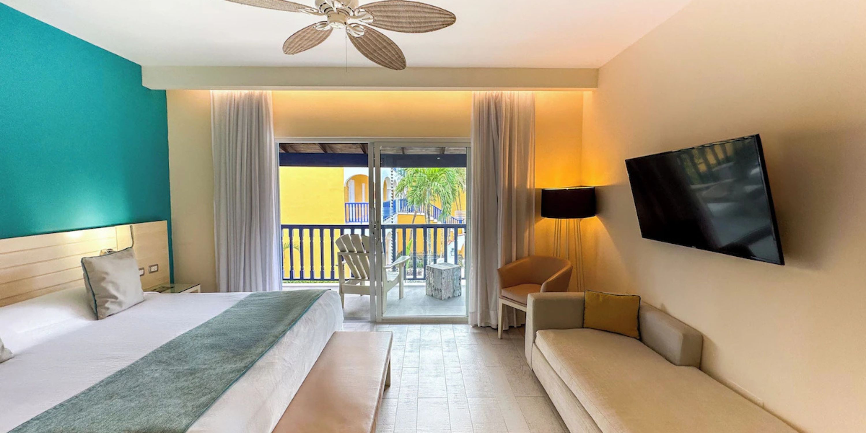 Modern room at Catalonia Bayahibe, perfect for a destination wedding, with bed, sofa, TV, and balcony.