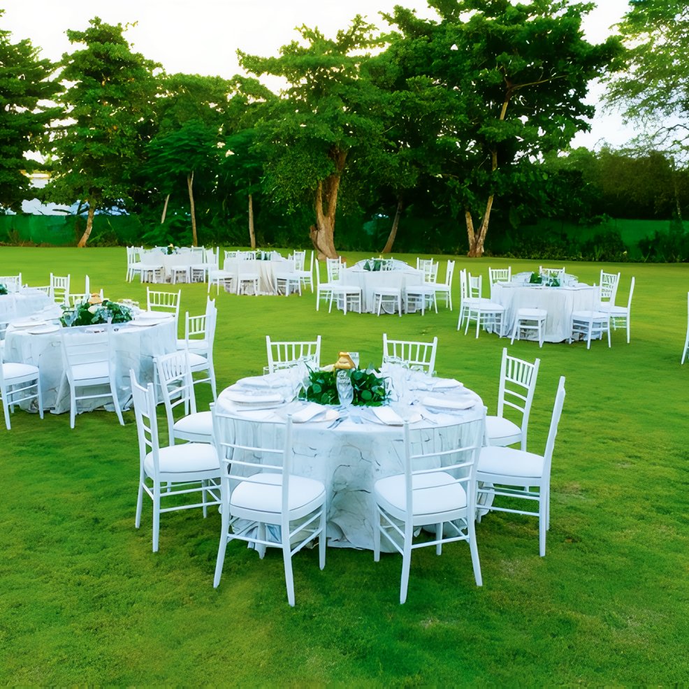 Round tables with white chairs arranged on a lush lawn, ready for a beautiful outdoor wedding event.