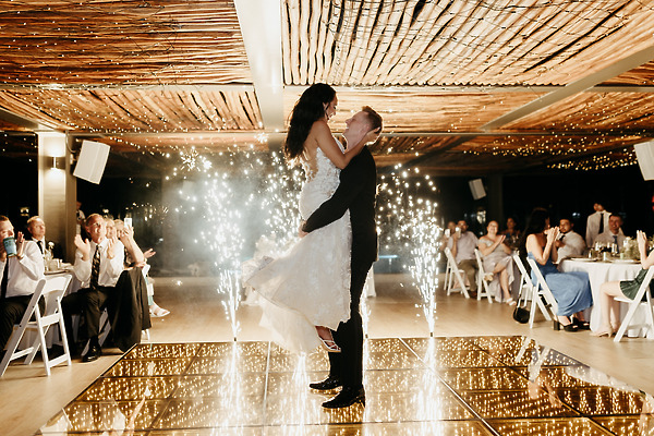 A groom lifts his bride on a glowing dance floor during their lively destination wedding celebration.