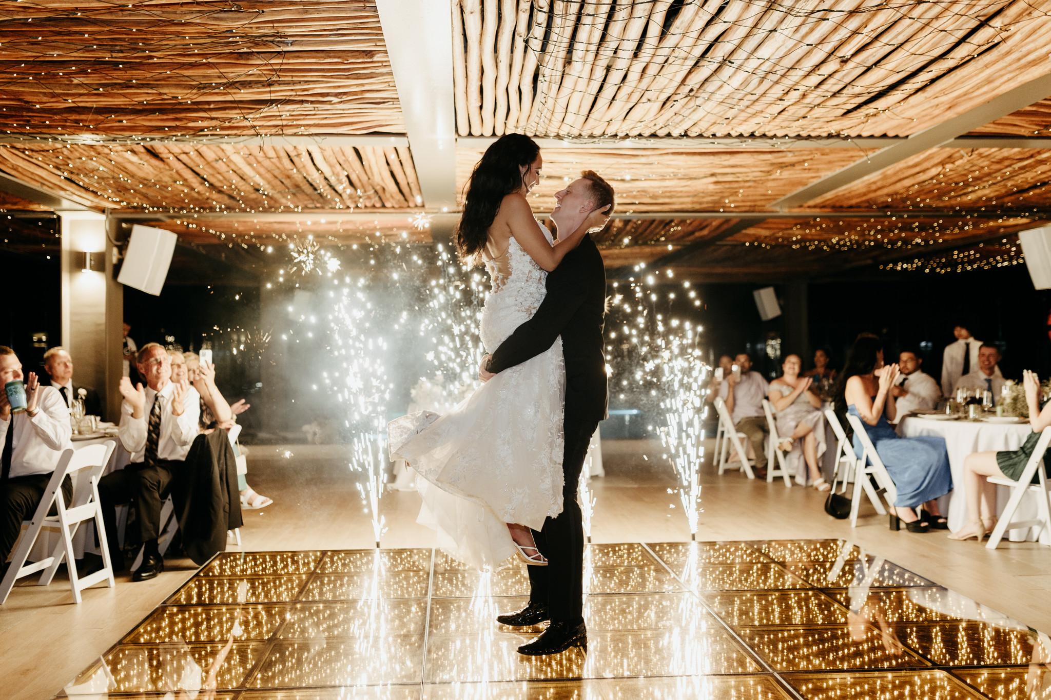 A groom lifts his bride on a glowing dance floor during their lively destination wedding celebration.
