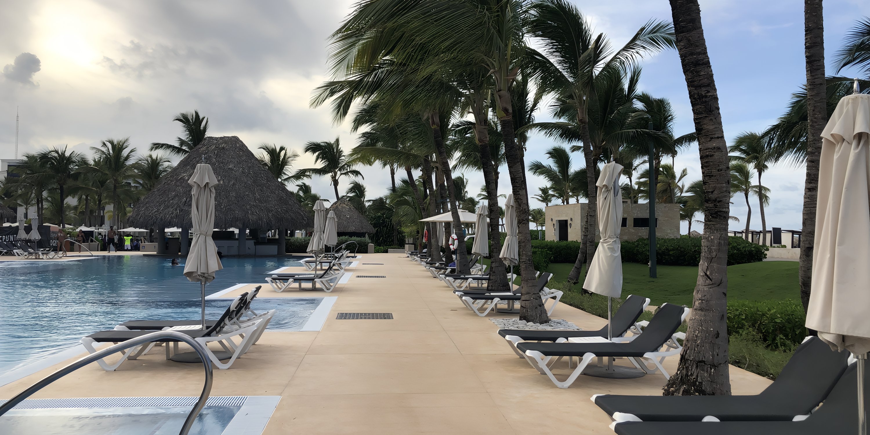 Lounge chairs by a large pool with palm trees and umbrellas, perfect for a destination wedding setting.