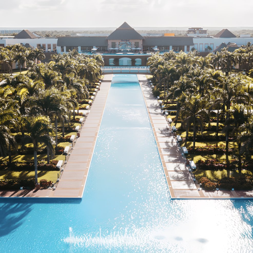 A long pool lined with palm trees creates a stunning path to a resort, perfect for a destination wedding.
