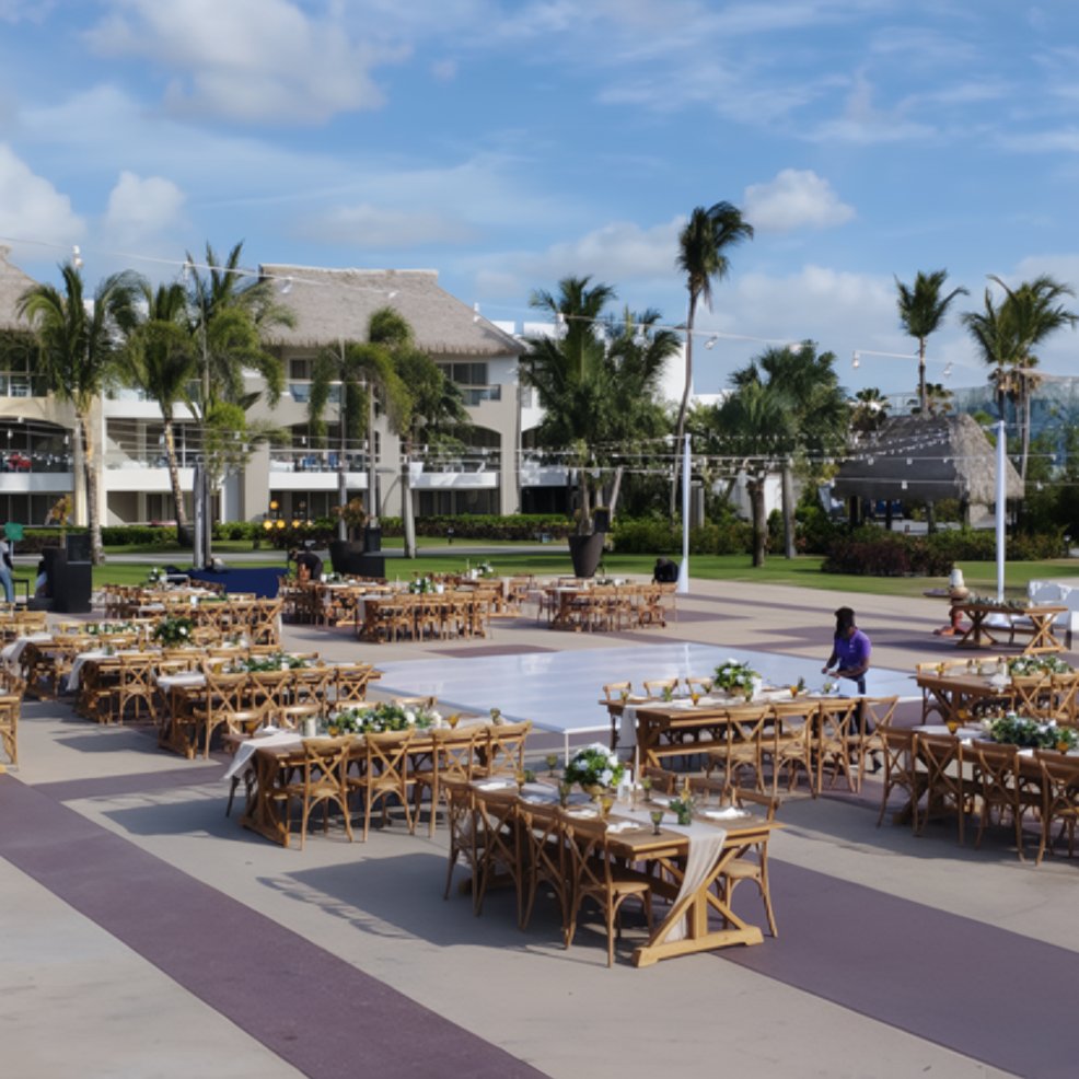 Destination wedding setup featuring decorated tables and chairs on a patio by palm trees and buildings.