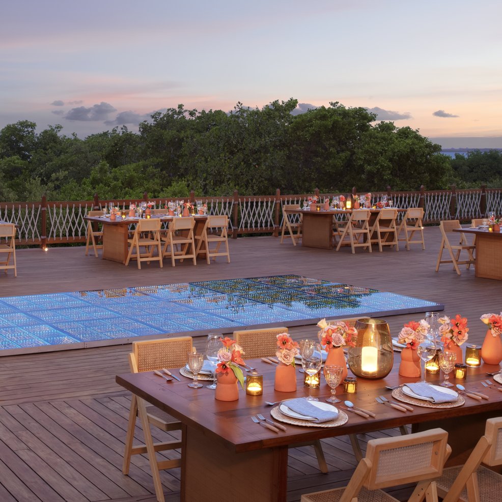 Elegant wedding dining setup with candlelit, decorated tables by a covered pool at sunset&mdash;perfect for a destination wedding.
