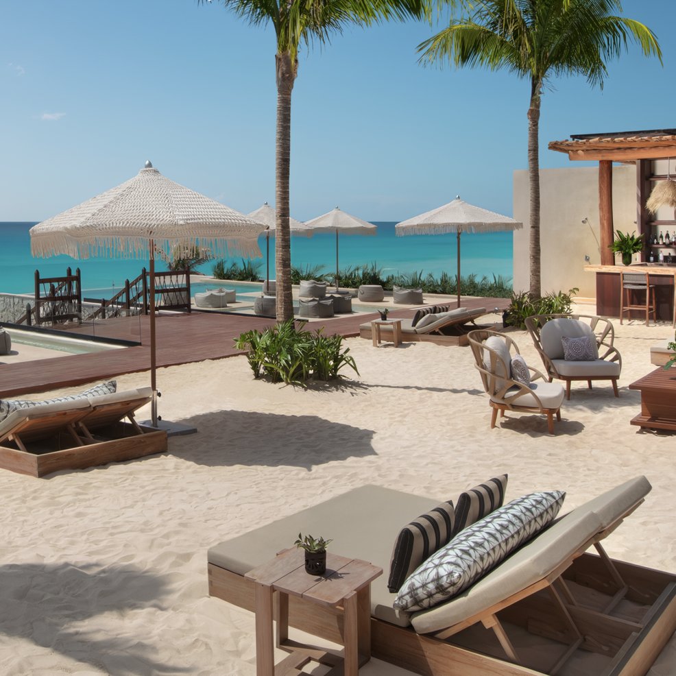 Beachside lounge perfect for a destination wedding, with sunbeds, umbrellas, palms, and an ocean-view bar.