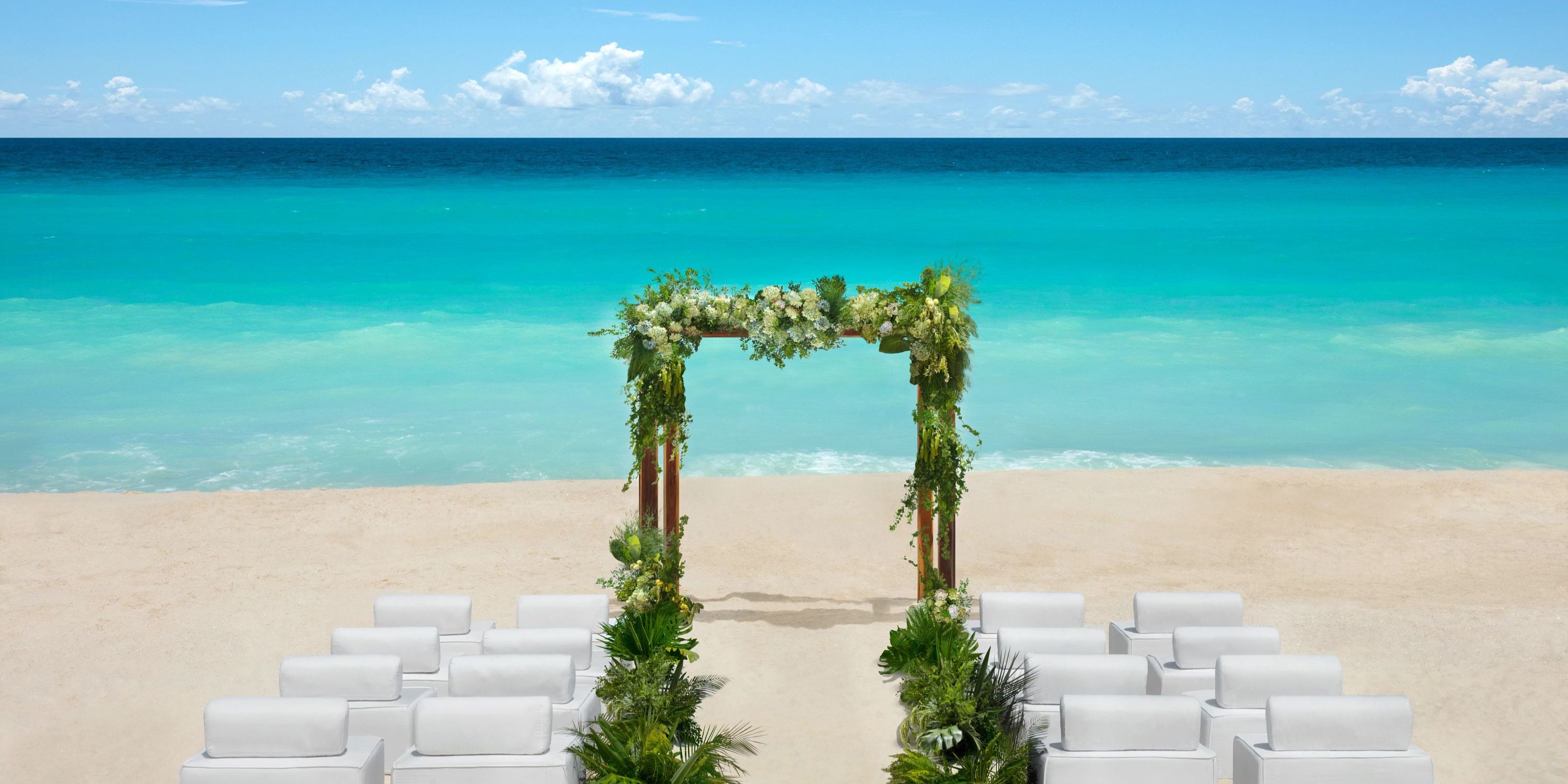 A wedding arch with white chairs arranged on the beach for a destination wedding at Hyatt Vivid Punta Cana.