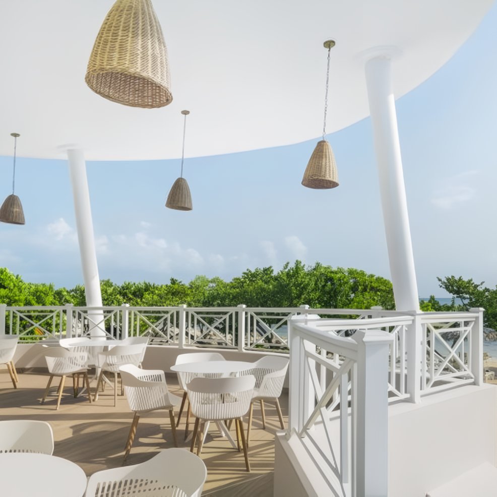 Chic outdoor patio set for a destination wedding, with white tables, chairs, and wicker pendant lights.