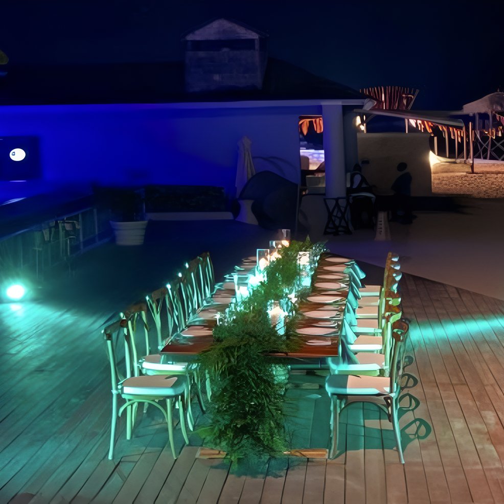 Long table set for a destination wedding dinner at night, glowing with blue and green lights.