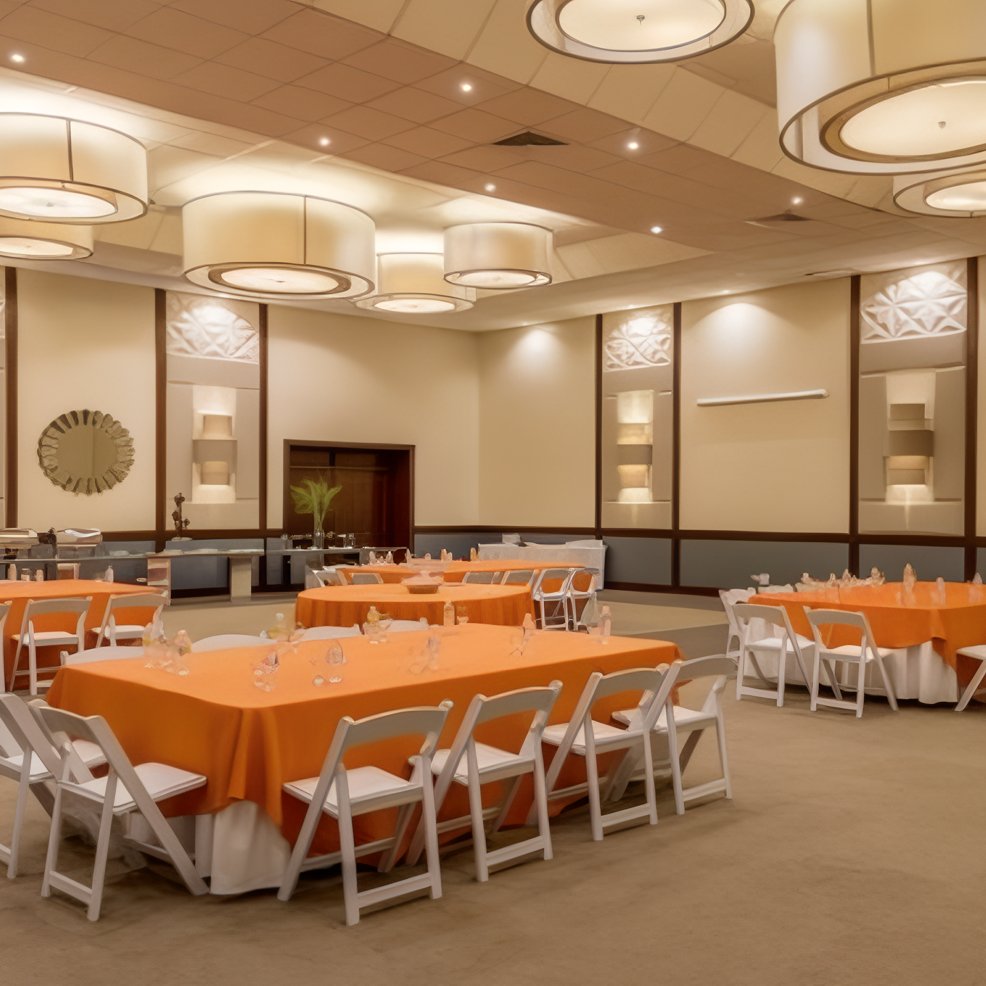Banquet hall set for a destination wedding, orange tablecloths, white chairs, and large ceiling lights.