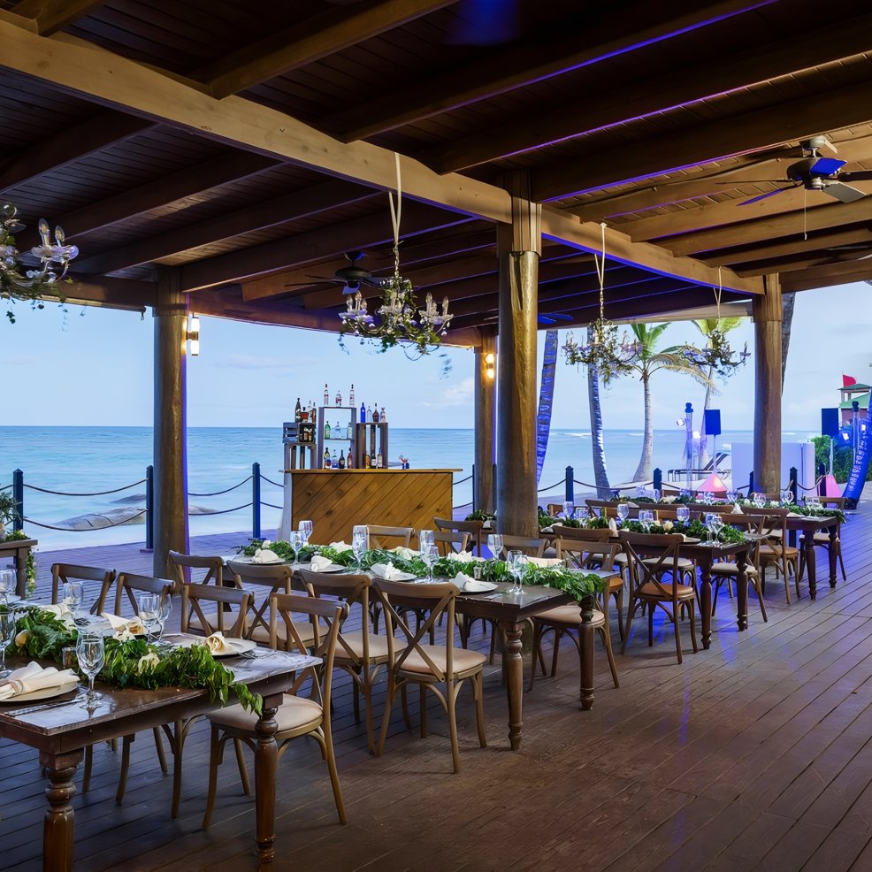 Open-air beachfront dining area with wooden tables, perfect for a destination wedding celebration.