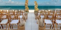 Wooden chairs set for a destination wedding face dried florals on the Ocean Allure Costa Mujeres terrace.