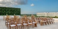 Wooden chairs arranged for a destination wedding outdoors at Ocean Allure Costa Mujeres, green wall behind.