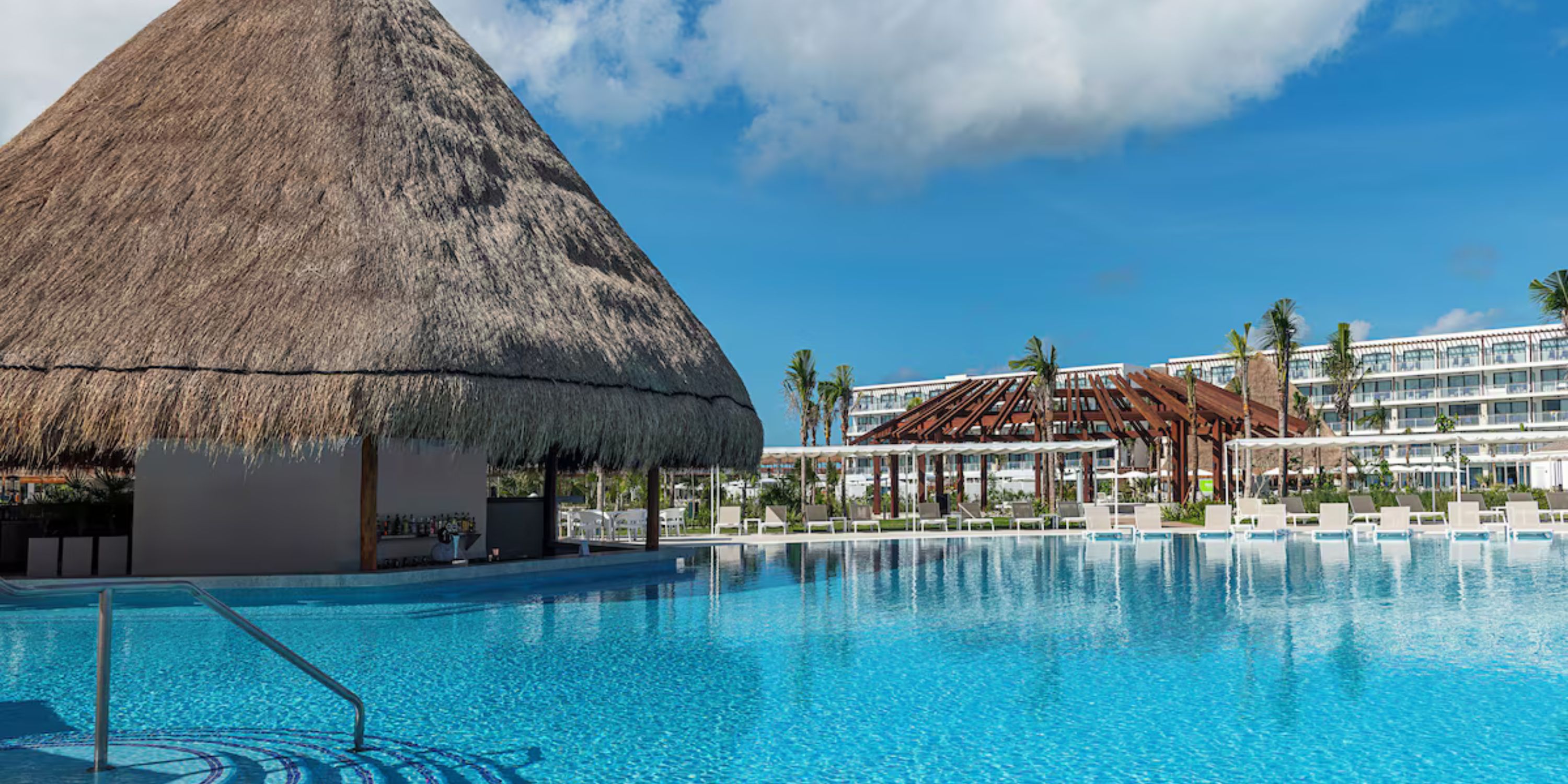 Large thatched-roof pool bar by the blue pool, perfect for a destination wedding at Ocean Coral and Turquesa.