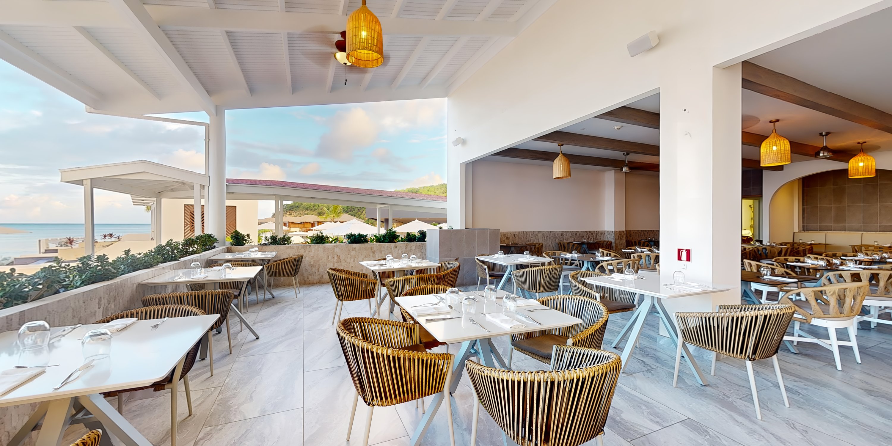 Modern open-air restaurant with wicker chairs and set tables, ideal for a destination wedding by the beach.
