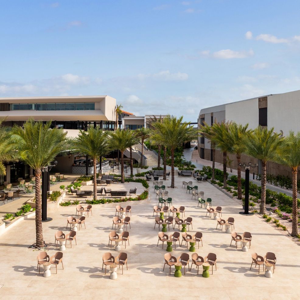 Outdoor courtyard with palm trees, perfect for a destination wedding, dotted with tables and chairs in sunlight.
