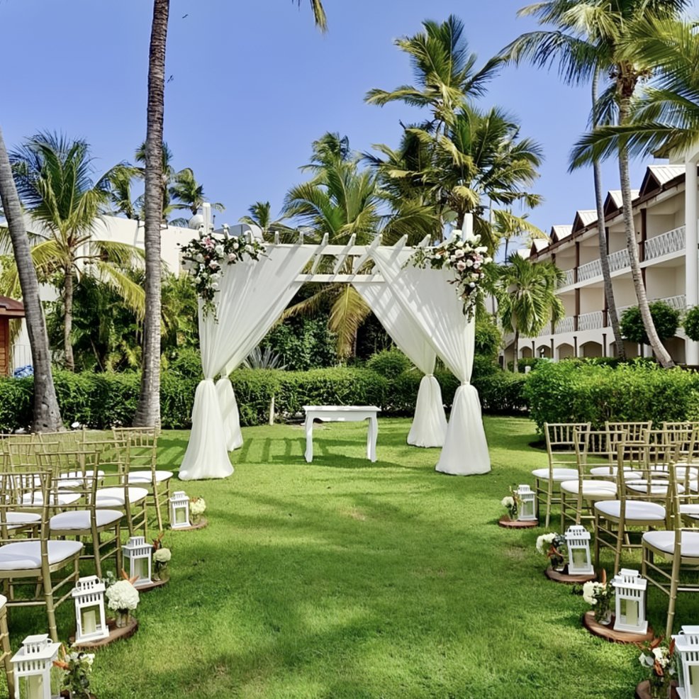 Destination wedding ceremony setup featuring a white draped archway, chairs, and lanterns on the grass.