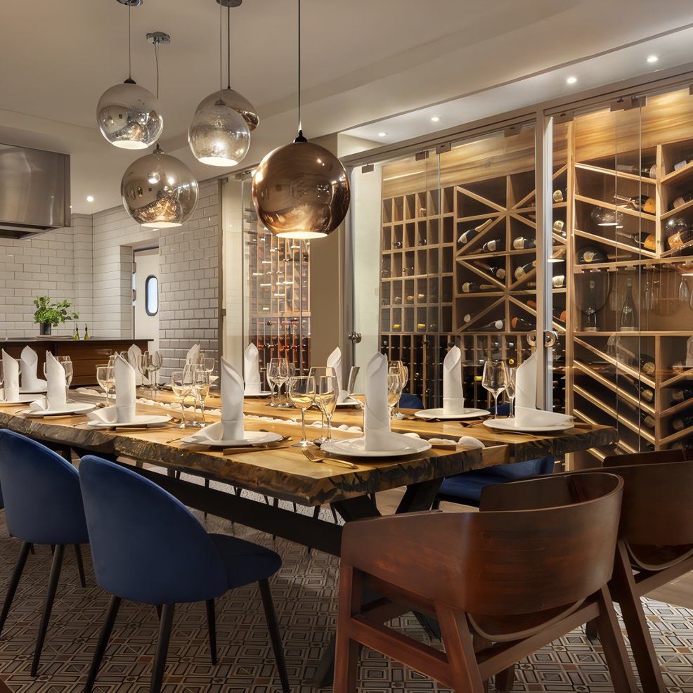 Elegant dining room set for a destination wedding, with blue chairs, wood accents, and glass wine wall.