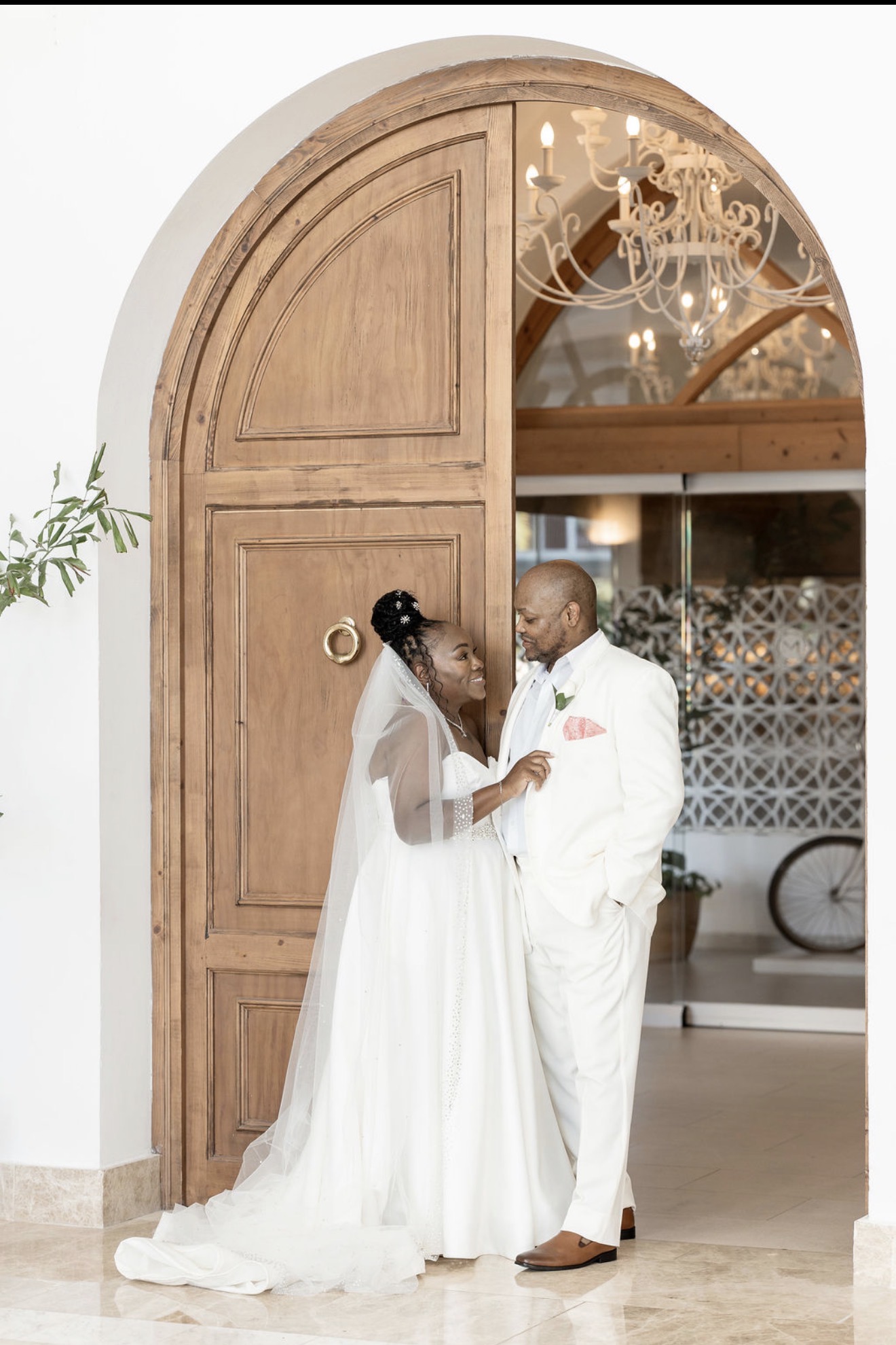 Catherine and Carlos smile together by a large arched wooden door at their destination wedding.