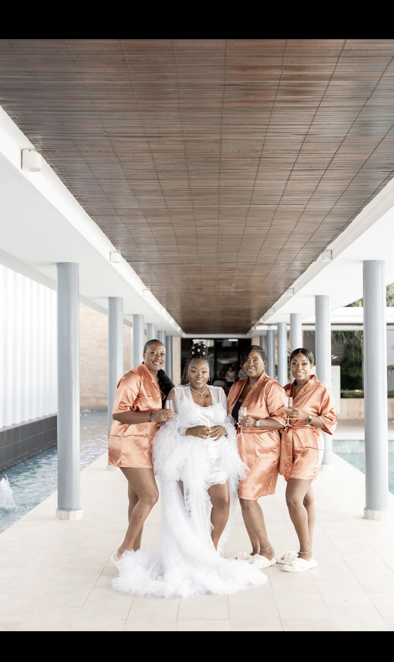 Bride in Catherine and Carlos gown with bridesmaids in satin robes at a destination wedding by the pool.