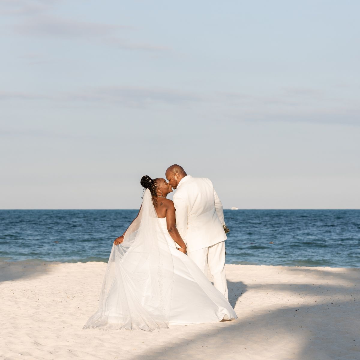 Catherine and Carlos share a kiss on the beach during their romantic destination wedding.
