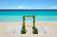 Destination wedding setup at Hyatt Vivid Punta Cana with white chairs and floral arch by turquoise water.