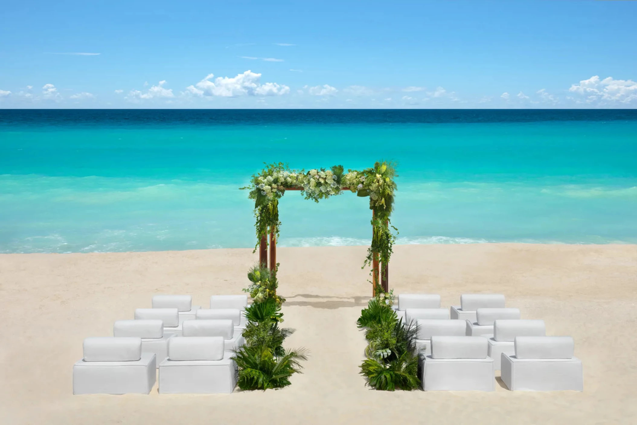 Destination wedding setup at Hyatt Vivid Punta Cana with white chairs and floral arch by turquoise water.