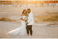 Tiffany and Anthony smile, holding flowers on the beach at sunset during their destination wedding.