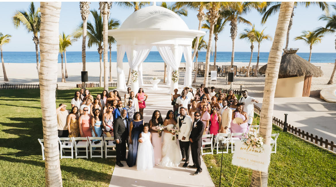 Tiffany and Anthony&rsquo;s destination wedding party poses by a white gazebo on the beach for a group photo.