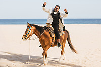 Tiffany and Anthony enjoy a destination wedding ride on a brown horse along the sandy ocean beach.