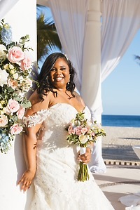 Tiffany and Anthony's destination wedding: Bride in white gown with bouquet by florals at beach venue.