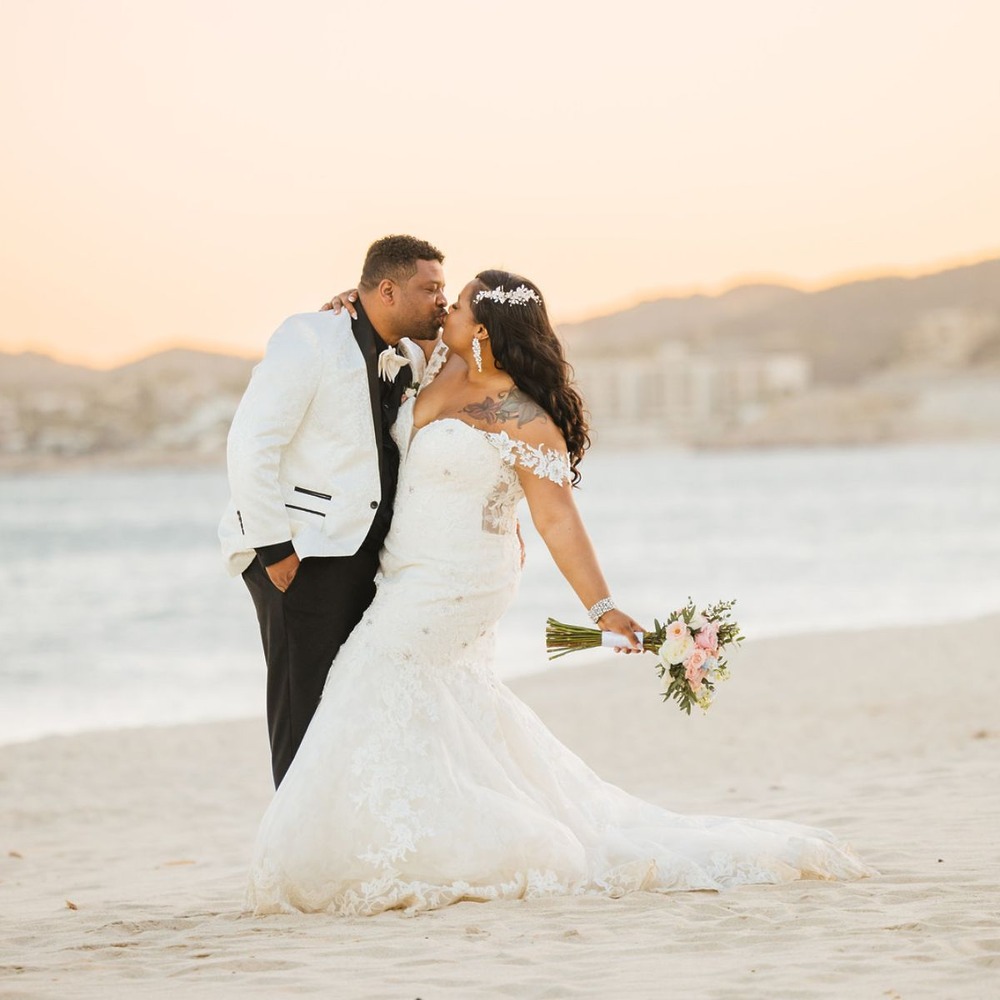 Tiffany and Anthony at their destination wedding, posing on a sunset beach as the bride holds her bouquet.