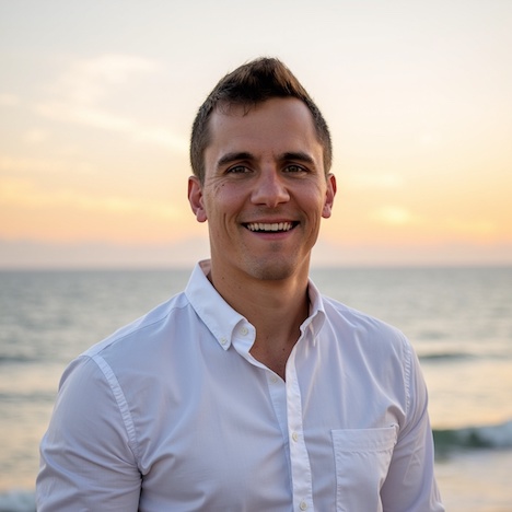 Man in a white shirt smiles on a beach at sunset, capturing a joyful moment at a destination wedding.