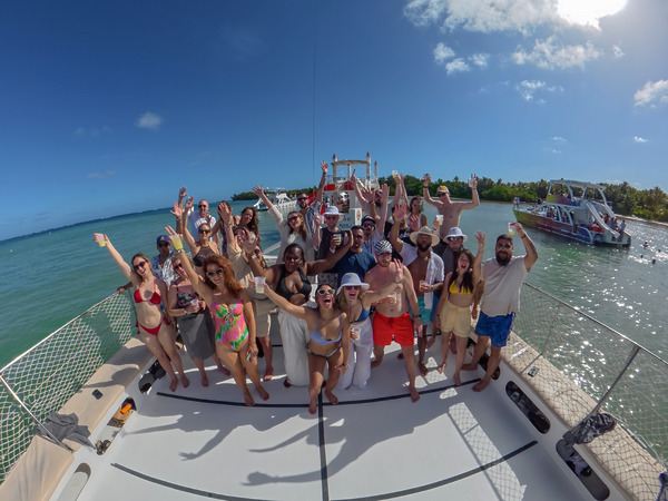 A group celebrates and poses on a boat deck in sunny, tropical waters during a destination wedding.