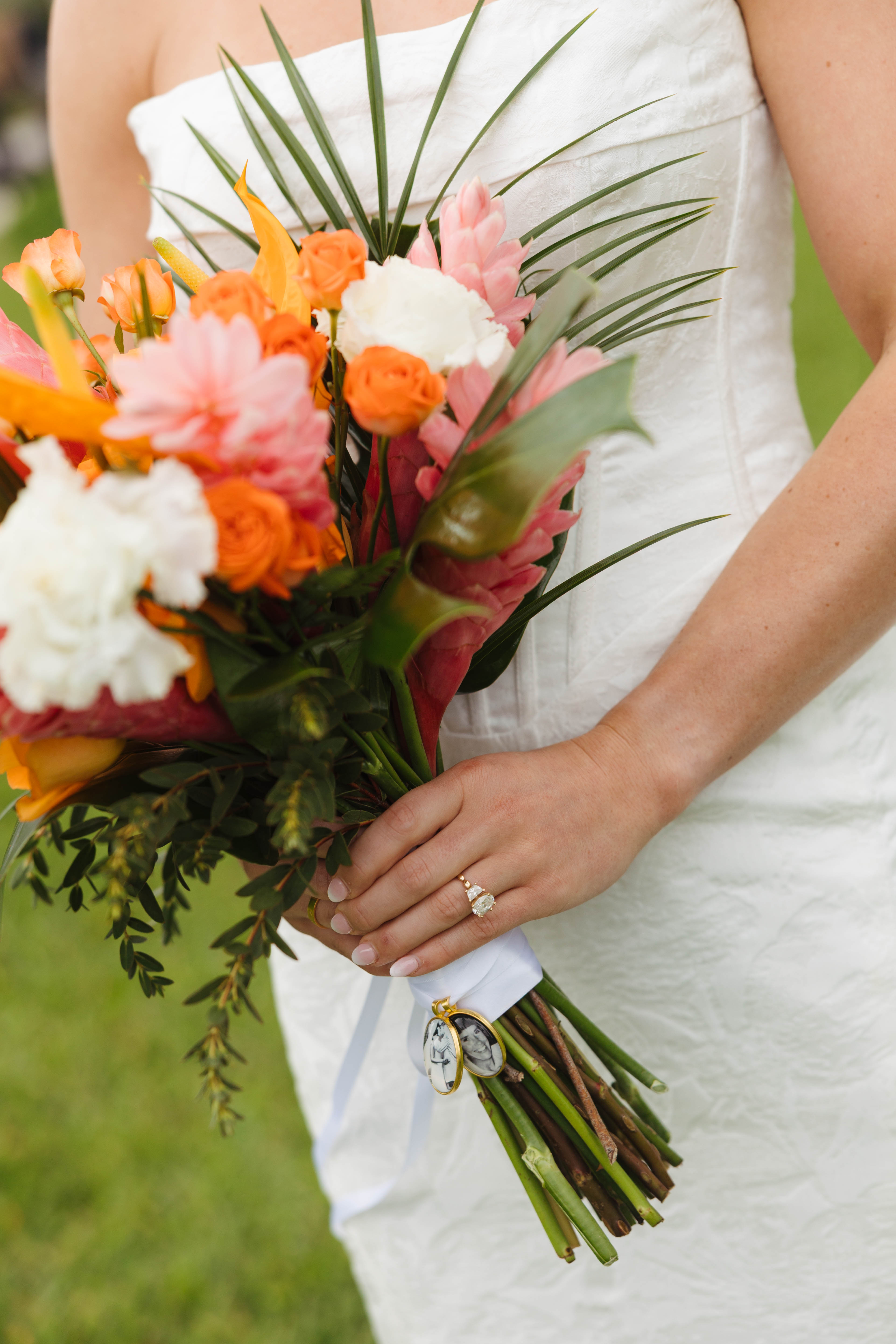 At a destination wedding, a bride in white displays her Tiffany and Anthony ring with a vibrant bouquet.