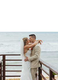 Tiffany and Anthony share a kiss during their destination wedding on a wooden deck by the ocean.