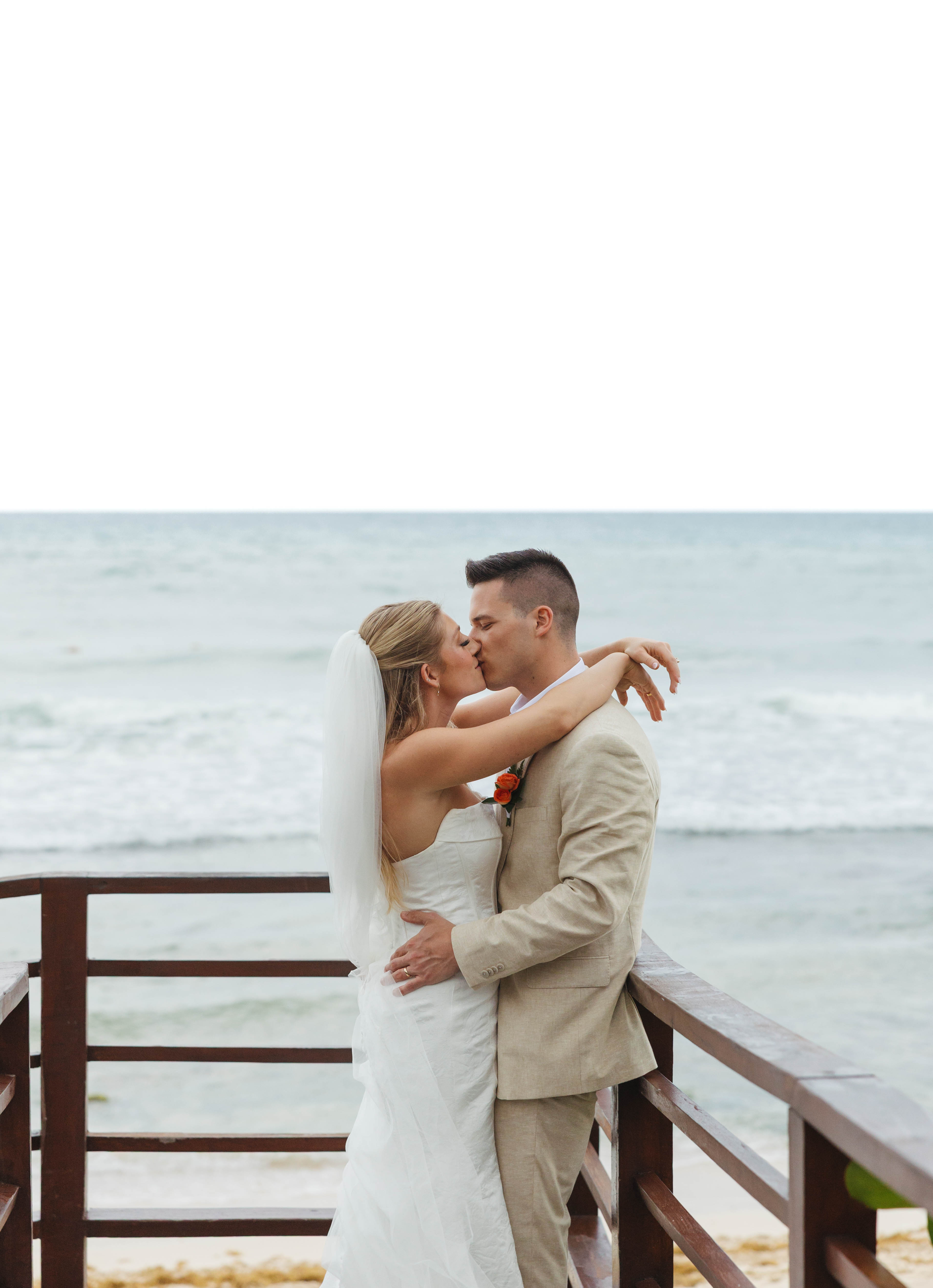 Tiffany and Anthony share a kiss during their destination wedding on a wooden deck by the ocean.
