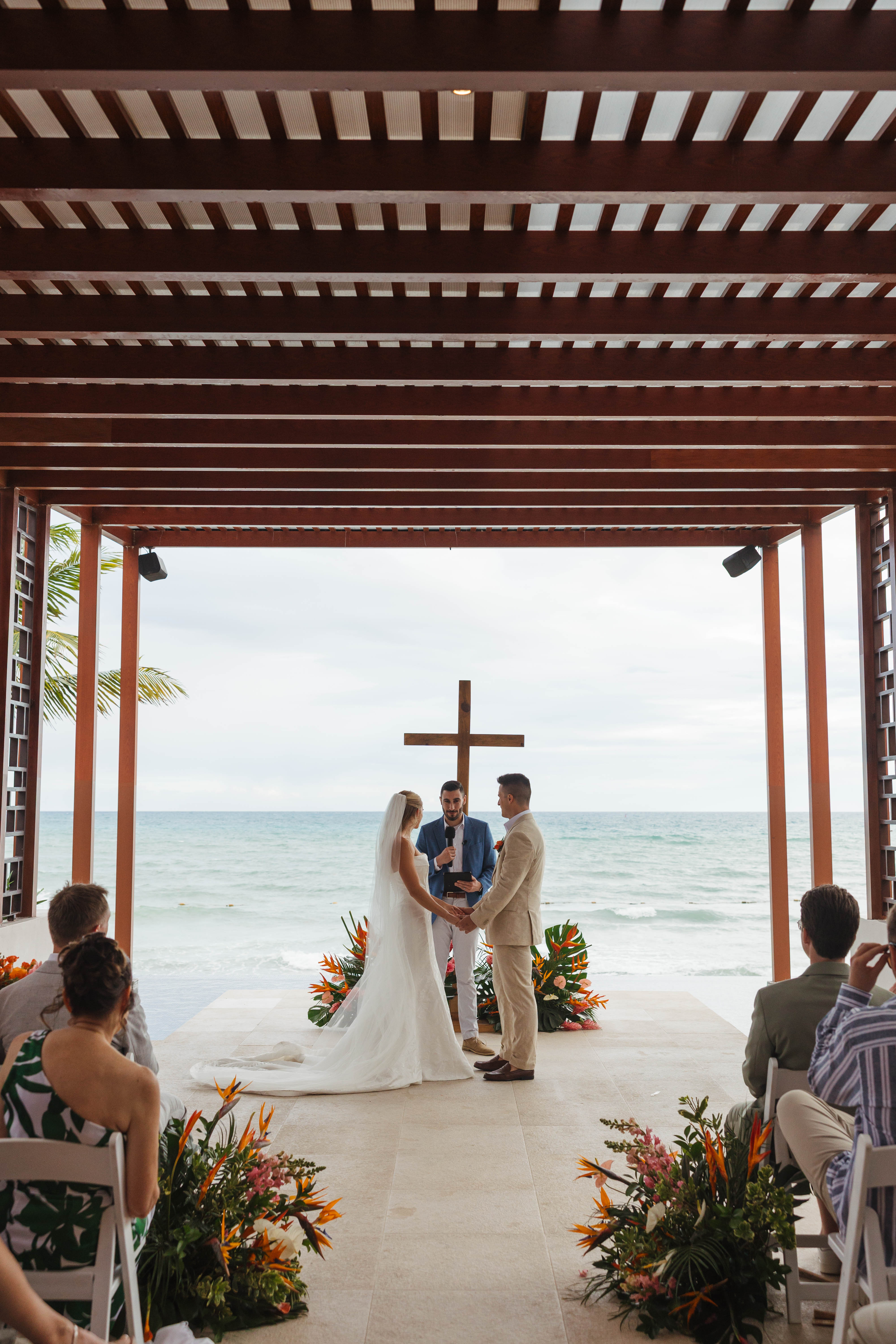 Tiffany and Anthony&rsquo;s destination wedding vows under a seaside pergola, guests seated close by.