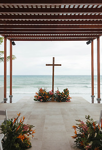 Wedding arch: wooden cross with floral decor under pergola, overlooking the ocean at a destination wedding.