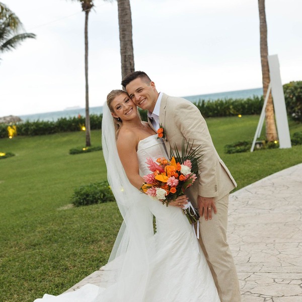 Tiffany and Anthony smiling and embracing outdoors at their destination wedding, holding colorful flowers.