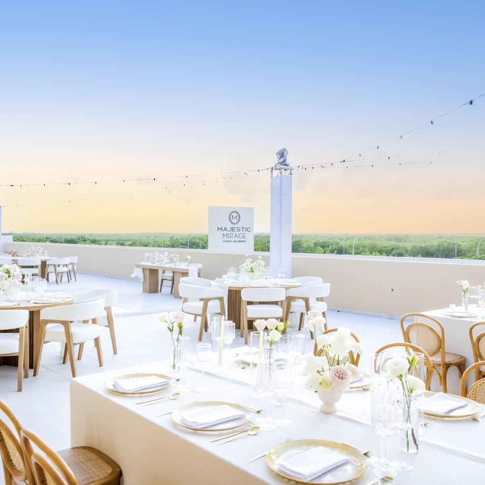 Rooftop destination wedding setup with white tables and chairs at sunset, Majestic Mirage sign visible.