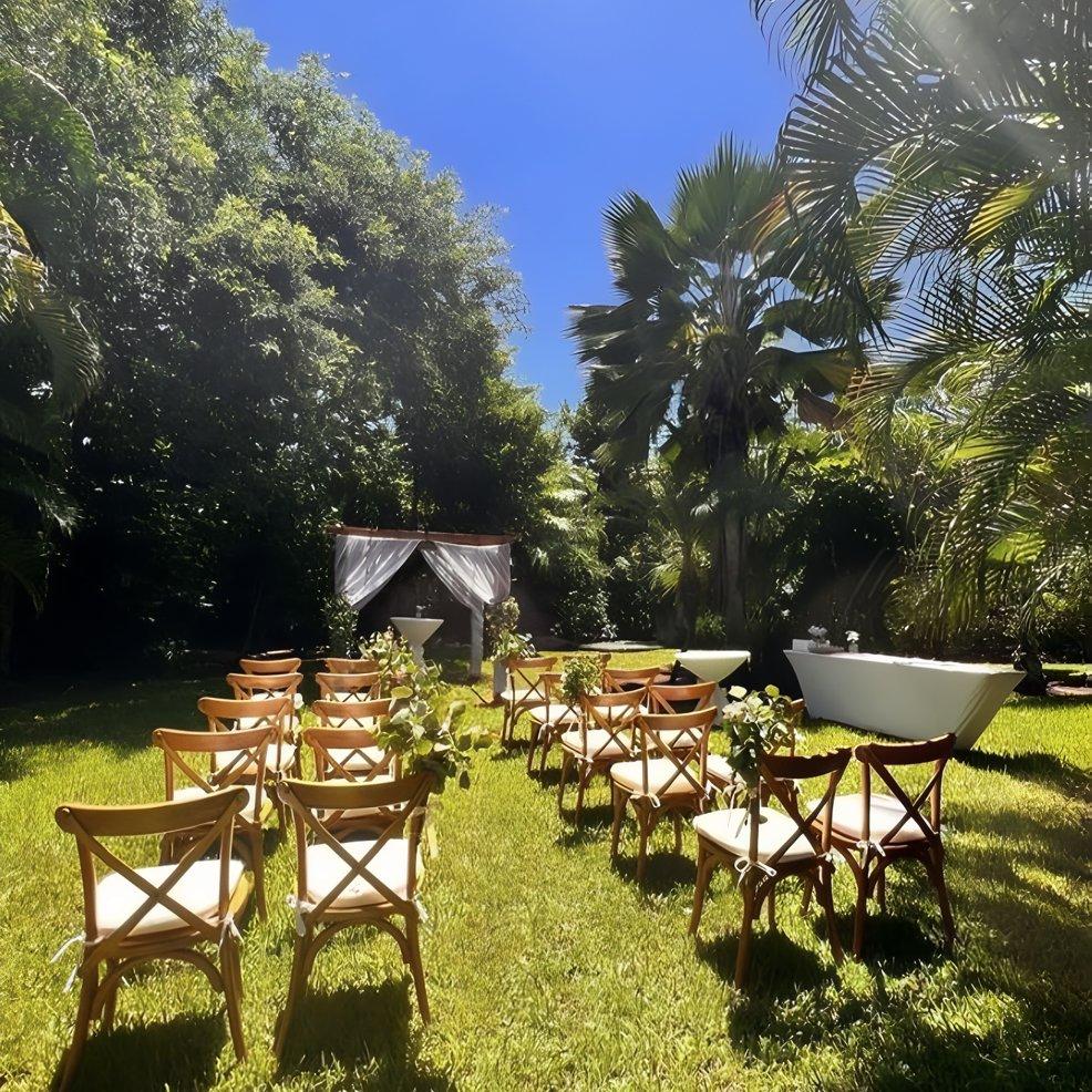 Destination wedding ceremony arranged outdoors, rows of chairs face a quaint altar beneath a blue sky.