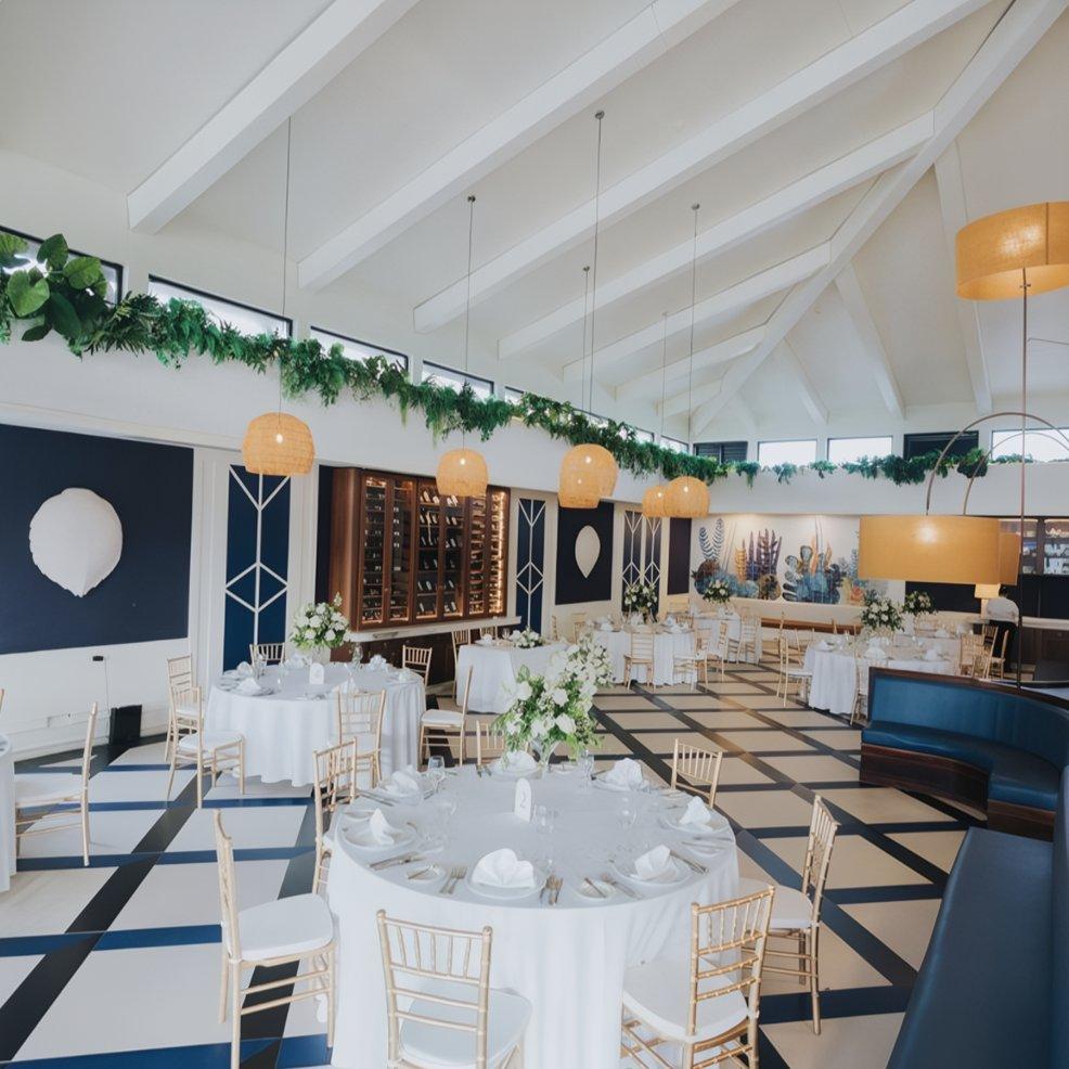 Elegant destination wedding hall featuring round tables, white linens, and lush greenery overhead.