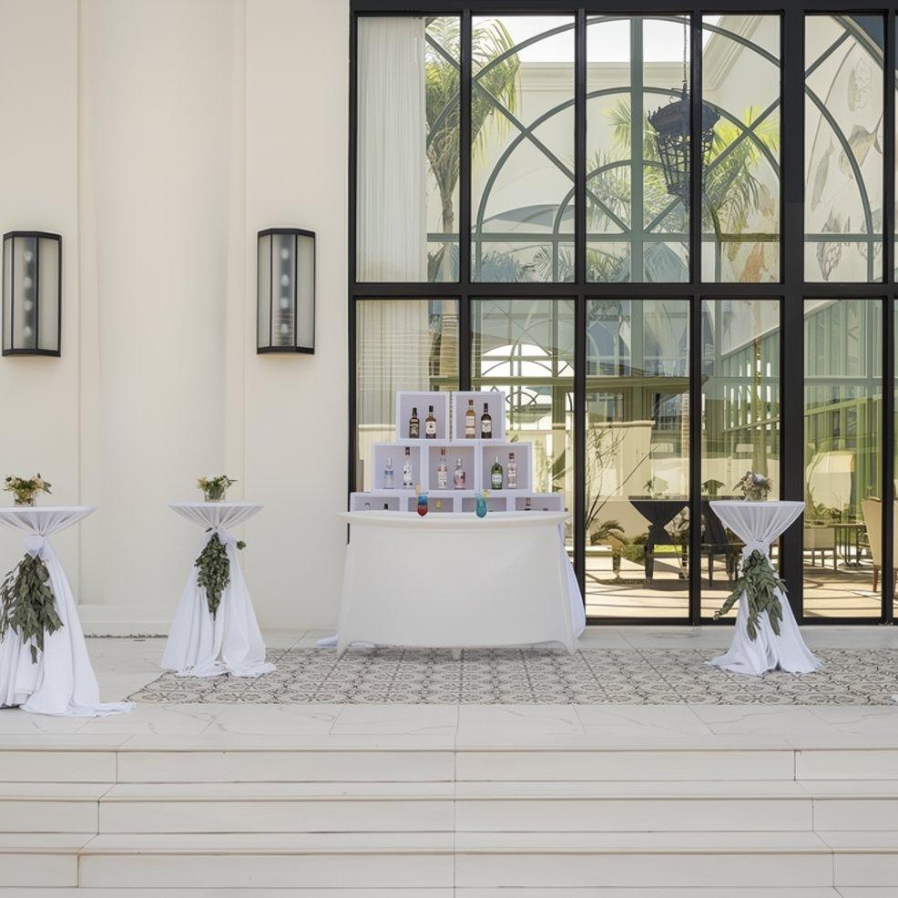 Outdoor bar setup at a destination wedding with bottles on display and cocktail tables draped in white cloths.