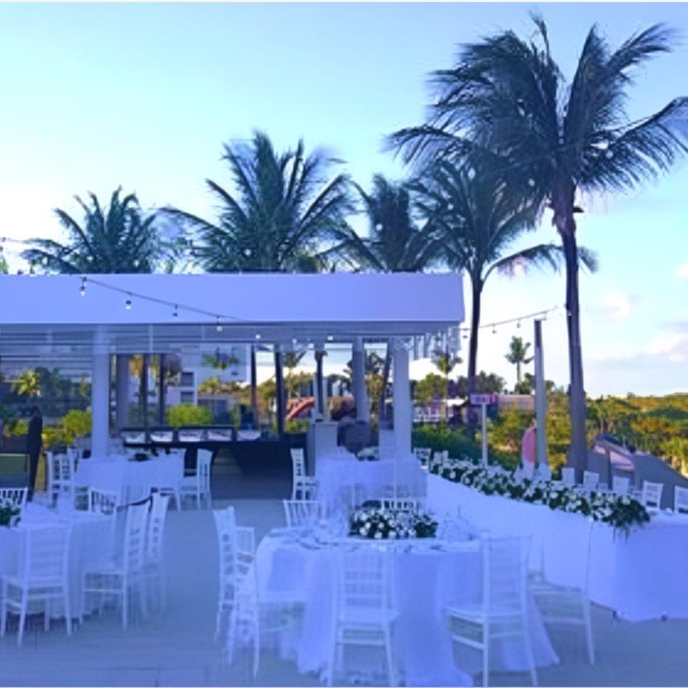 Destination wedding reception outdoors featuring white tables and chairs, palm trees, and string lights.
