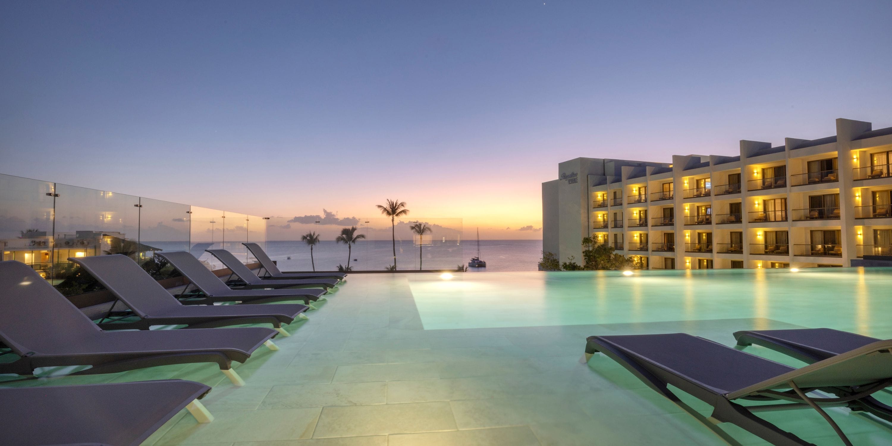 Infinity pool at Royalton Vessence Barbados, ideal for sunset weddings, features lounge chairs.