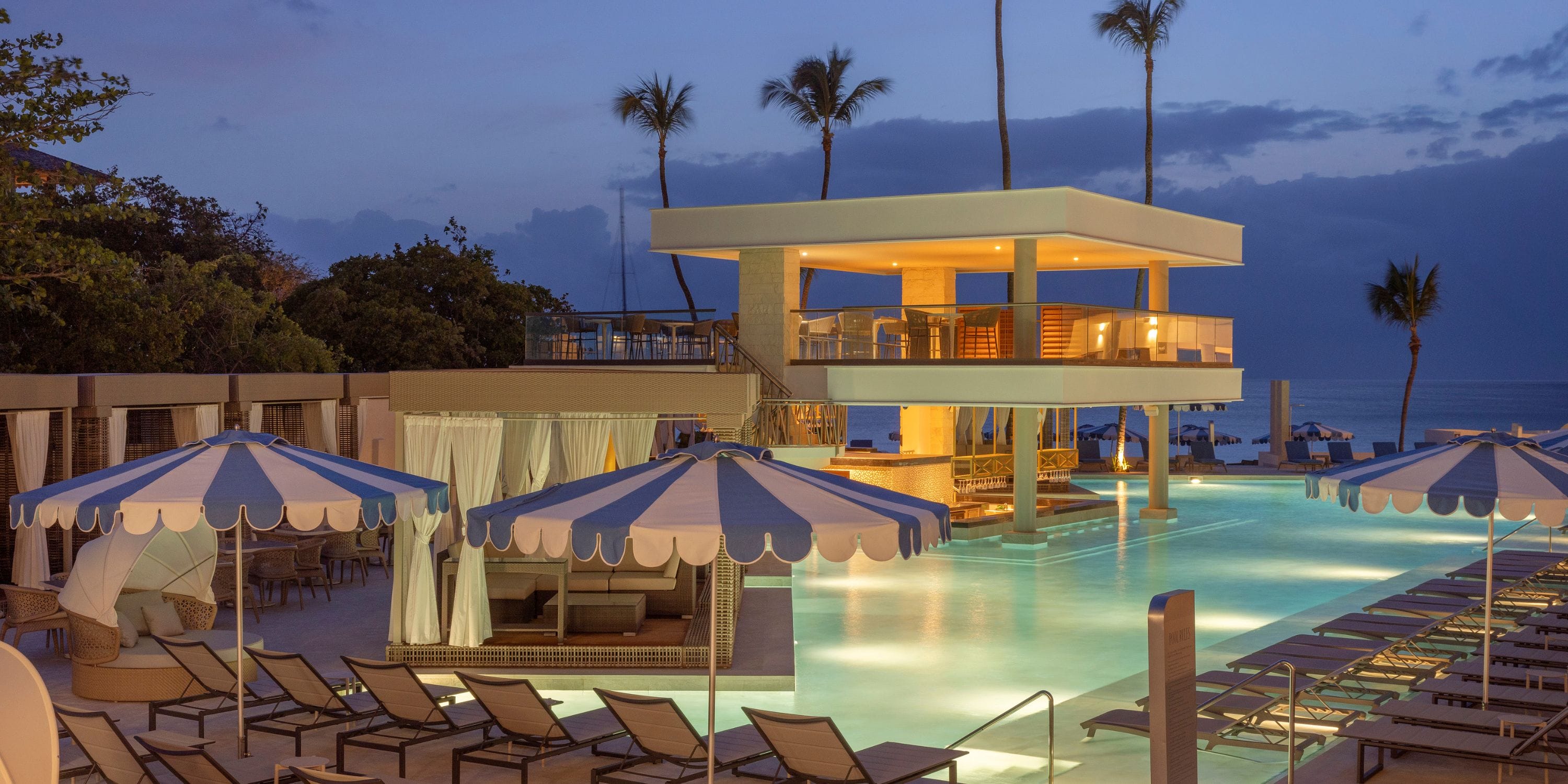 Royalton Vessence Barbados: ideal destination wedding scene with lit pool, cabanas & ocean at dusk.