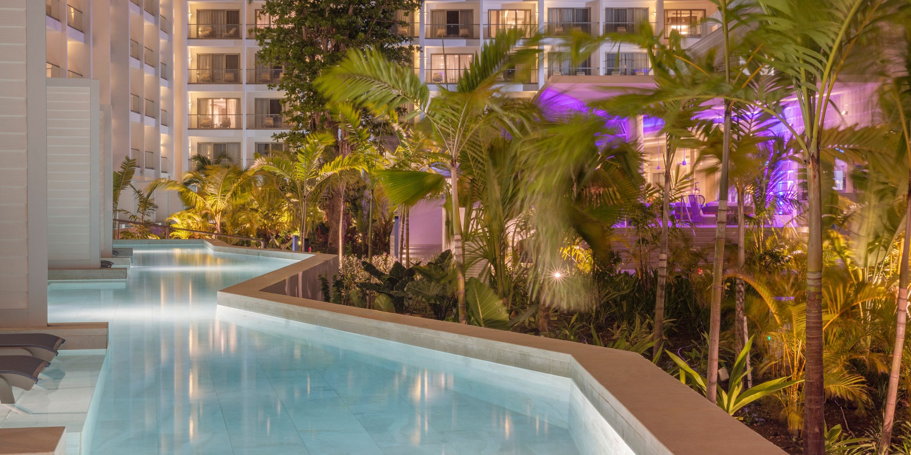 Night view of Royalton Vessence Barbados pool, ideal for a destination wedding amid palm trees.