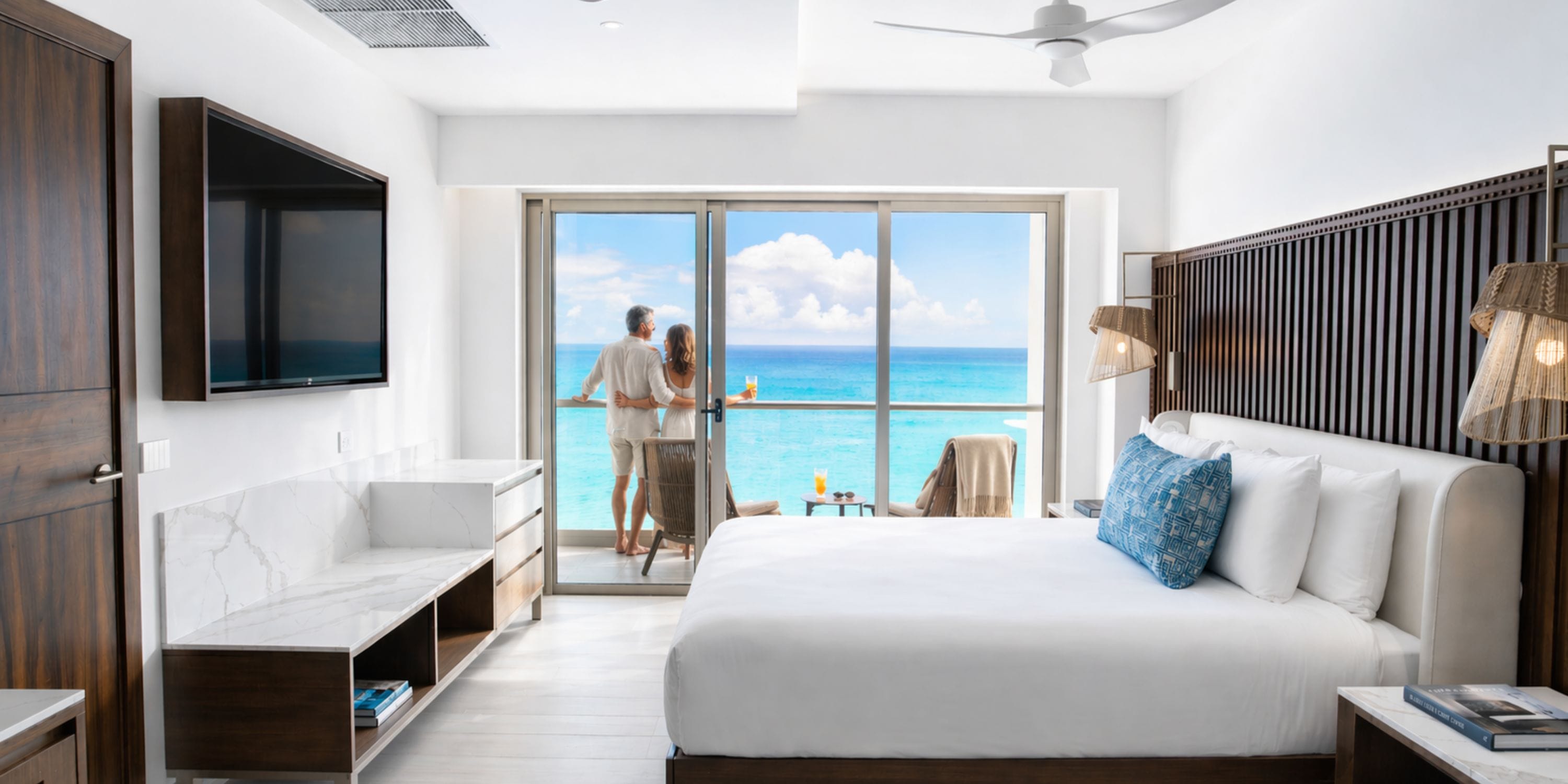 Ocean-view room at Royalton Vessence Barbados; two guests enjoy the sea from a destination wedding balcony.